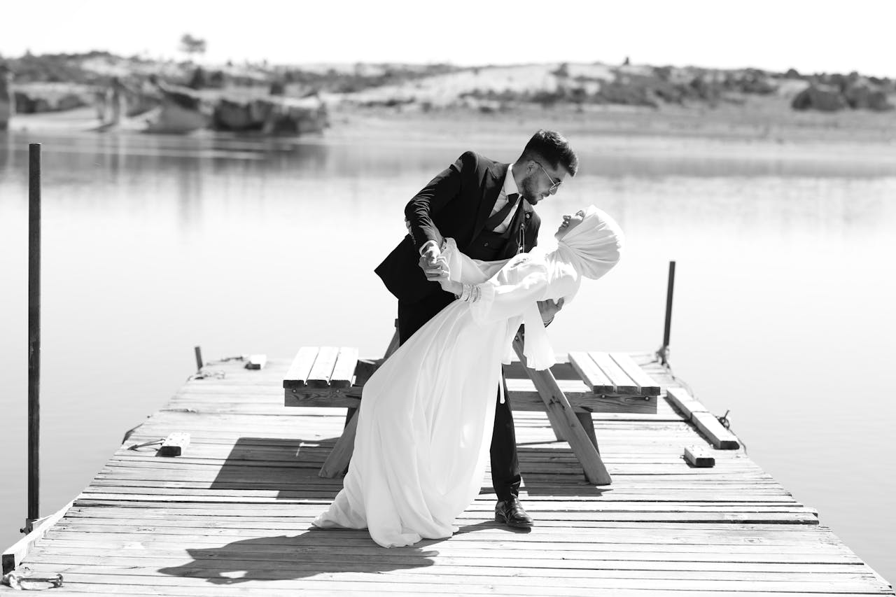 A couple in formal attire dances on a dock by a serene lake, exuding elegance and romance.